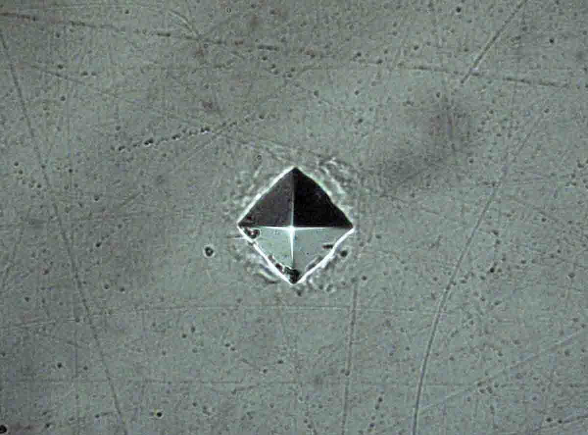 This is a fully-lit indent in a brass sample to illustrate the pyramid shape of the indenter, magnified 500 times.